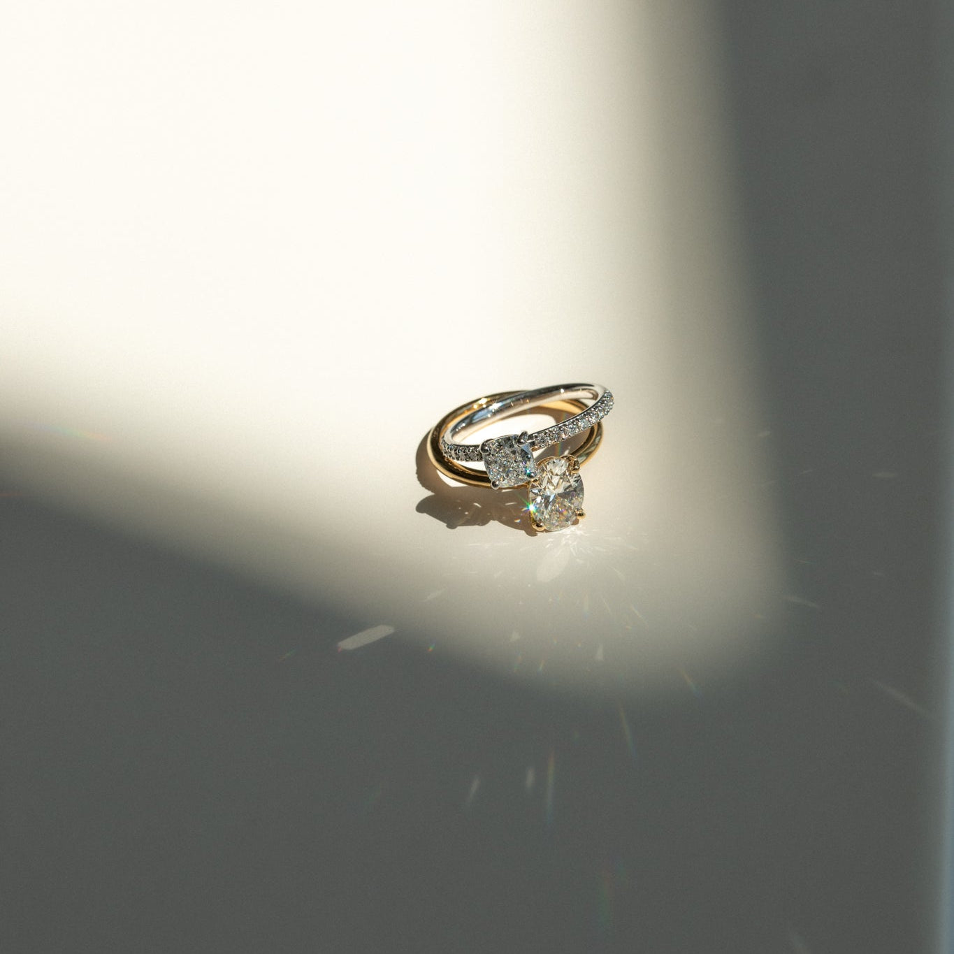 Gold engagement ring with an oval diamond centerpiece and accent stones, illuminated by a spotlight on a light surface.