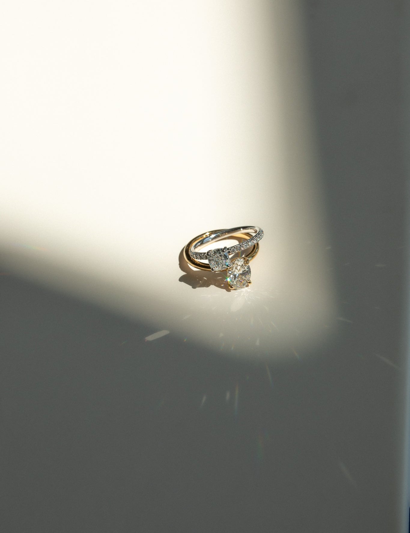 Gold engagement ring with an oval diamond centerpiece and accent stones, illuminated by a spotlight on a light surface.