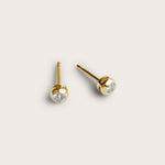 A pair of gold stud earrings featuring small, round diamond stones set in a smooth, rounded bezel setting. The earrings are simple yet elegant, with the diamonds subtly placed at the center.