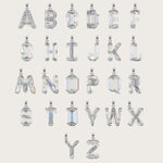 Set of silver alphabet pendants with sparkling gemstones in various cuts, arranged alphabetically on a light beige background.