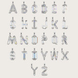 Set of silver alphabet pendants with sparkling gemstones in various cuts, arranged alphabetically on a light beige background.