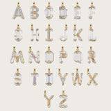 Set of gold alphabet pendants with sparkling gemstones in various cuts, arranged alphabetically on a light beige background.