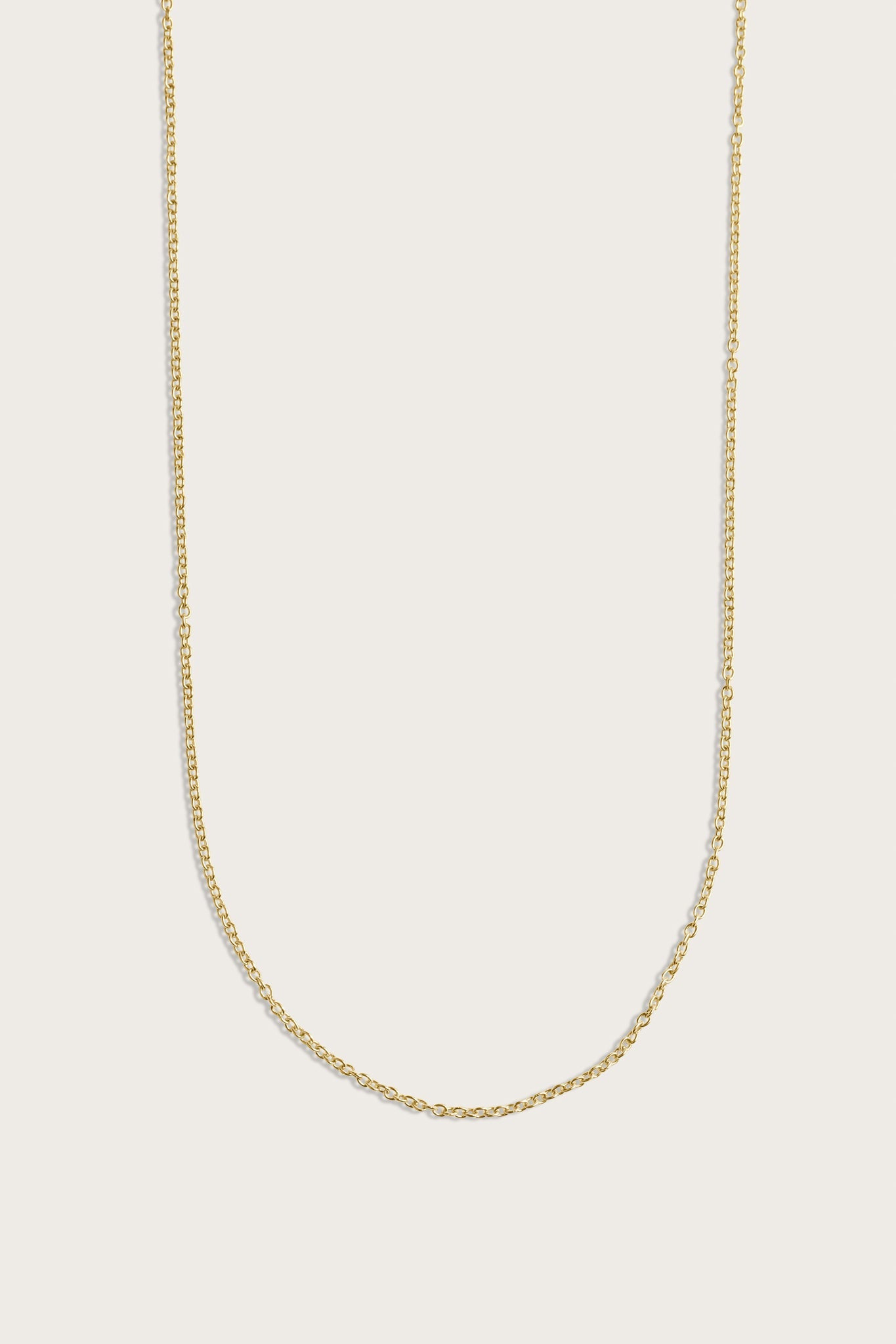 Simple gold chain necklace displayed on a light beige background.