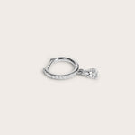 Silver hoop earring adorned with pavé-set diamonds and a dangling pear-shaped diamond, displayed on a light beige background.