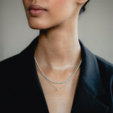 An elegant editorial lifestyle portrait of a model wearing a blazer, showcasing a luxury layering combination with a white gold bezel-set diamond necklace layered beneath a shimmering rose gold diamond tennis necklace.