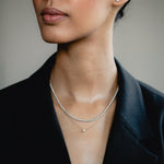 An elegant editorial lifestyle portrait of a model wearing a blazer, showcasing a luxury layering combination with a yellow gold bezel-set diamond necklace layered beneath a shimmering white gold diamond tennis necklace.