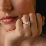 Close-up of the KARAAT Emerald and Pear Toi et Moi diamond ring in yellow gold, hand raised to the model's lips