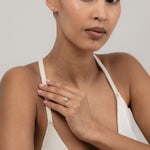 An editorial portrait of a model wearing a rose strap top, elegantly displaying a yellow gold KARAAT emerald-shaped diamond solitaire ring stacked with a gold band on her finger.