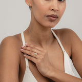 An editorial portrait of a model wearing a rose strap top, elegantly displaying a yellow gold KARAAT emerald-shaped diamond solitaire ring stacked with a gold band on her finger.