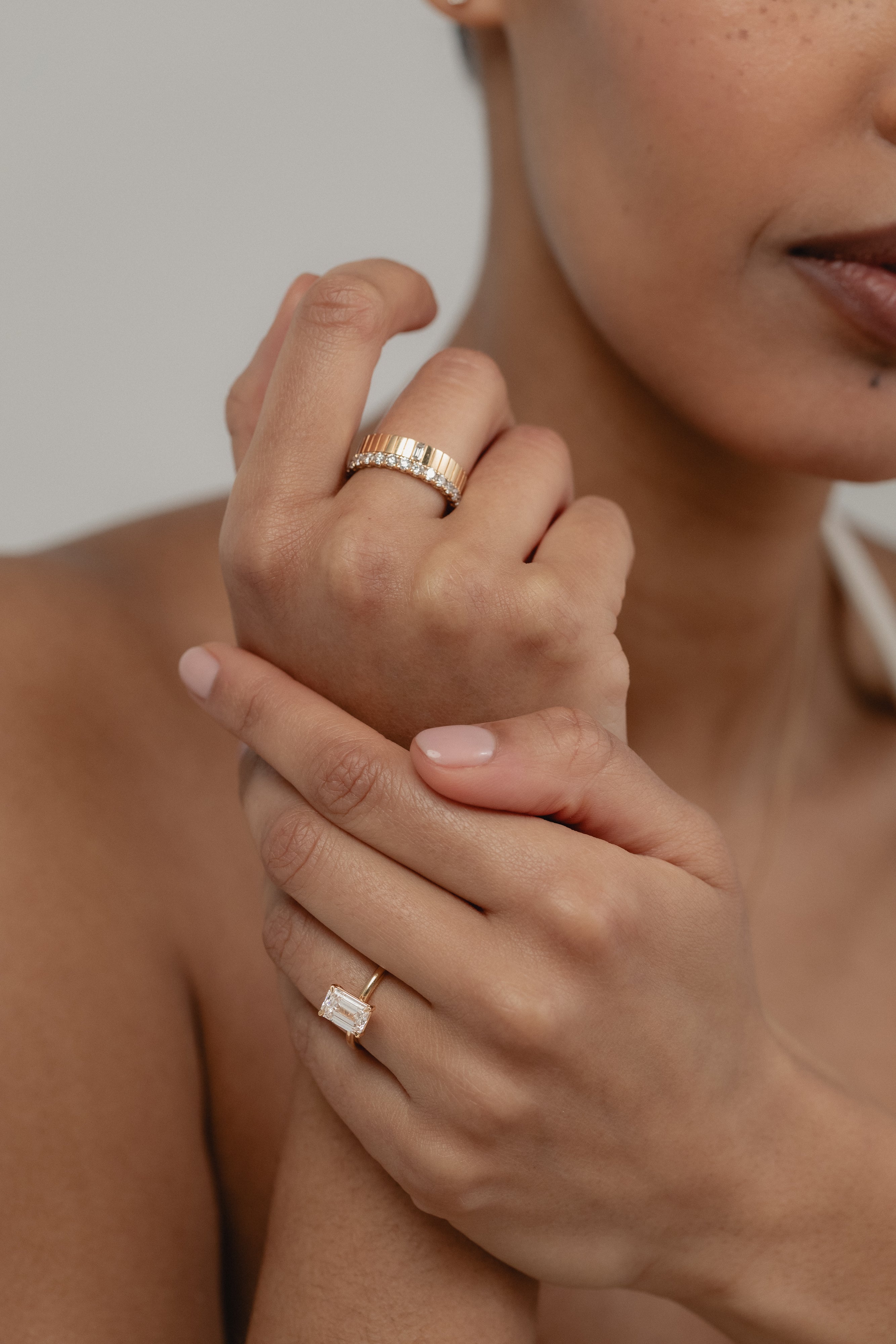 A beautiful shot of a model's crossed hands, styled with a white gold KARAAT emerald-cut solitaire ring on her ring finger and a bold ring stack on her index finger.