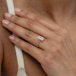 A close-up view of a model's hand showcasing the exquisite profile and setting of a KARAAT emerald-cut solitaire diamond engagement ring in 18k yellow gold.