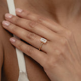 A close-up view of a model's hand showcasing the exquisite profile and setting of a KARAAT emerald-cut solitaire diamond engagement ring in 18k yellow gold.