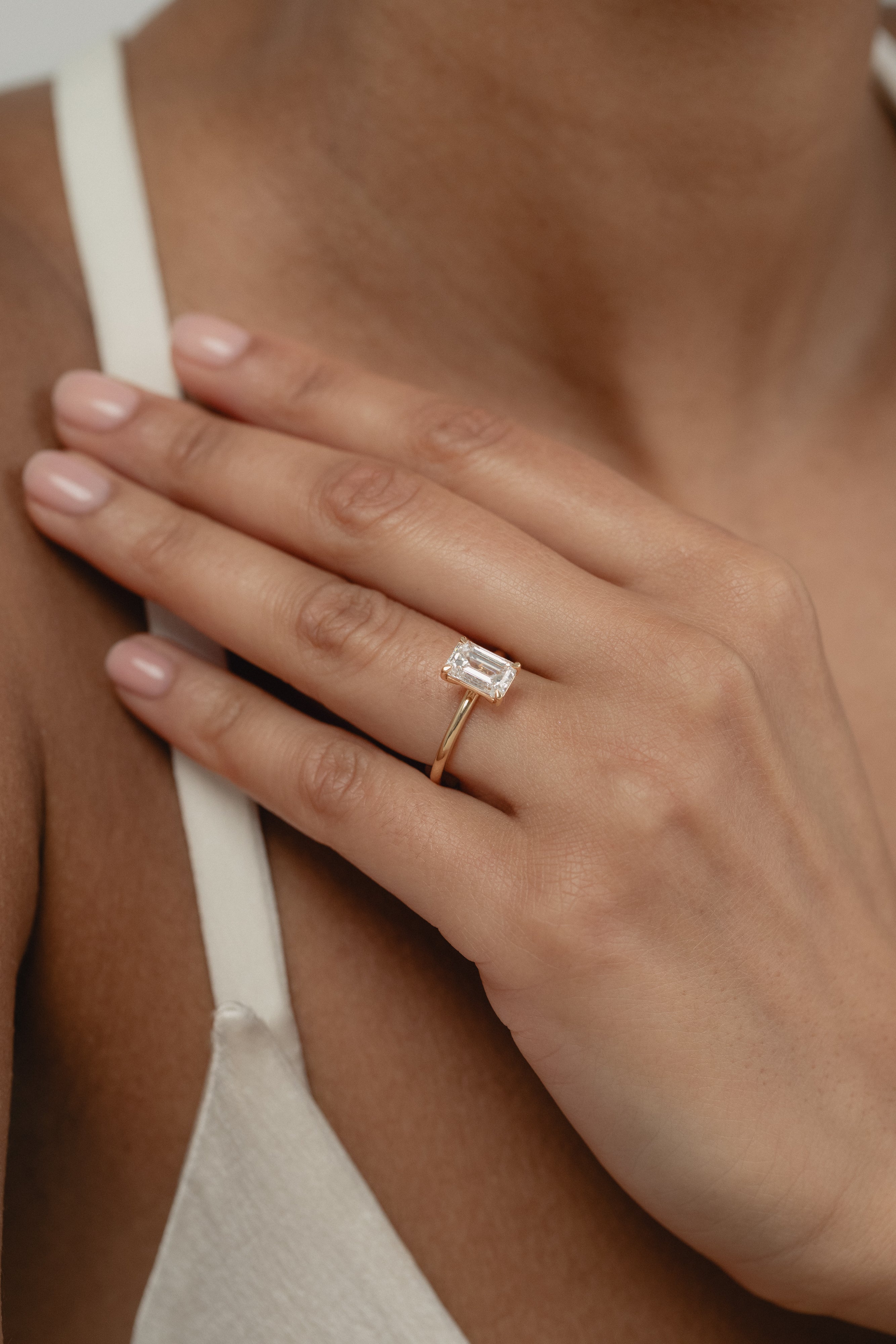 A close-up view of a model's hand showcasing the exquisite profile and setting of a KARAAT emerald-cut solitaire diamond engagement ring in 18k yellow gold.