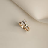 Still life shot of a luxury bridal ring stack featuring a classic oval solitaire diamond engagement ring paired flush with the Pavé Diamond Ring II on a cream fabric background.