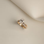 Still life shot of a white gold luxury bridal ring stack featuring a classic oval solitaire diamond engagement ring paired flush with the Pavé Diamond Ring II on a cream fabric background.