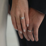 A close-up of a couple’s hands celebrating an engagement, featuring a KARAAT Oval Solitaire diamond ring with a pavé band in 18k yellow gold.
