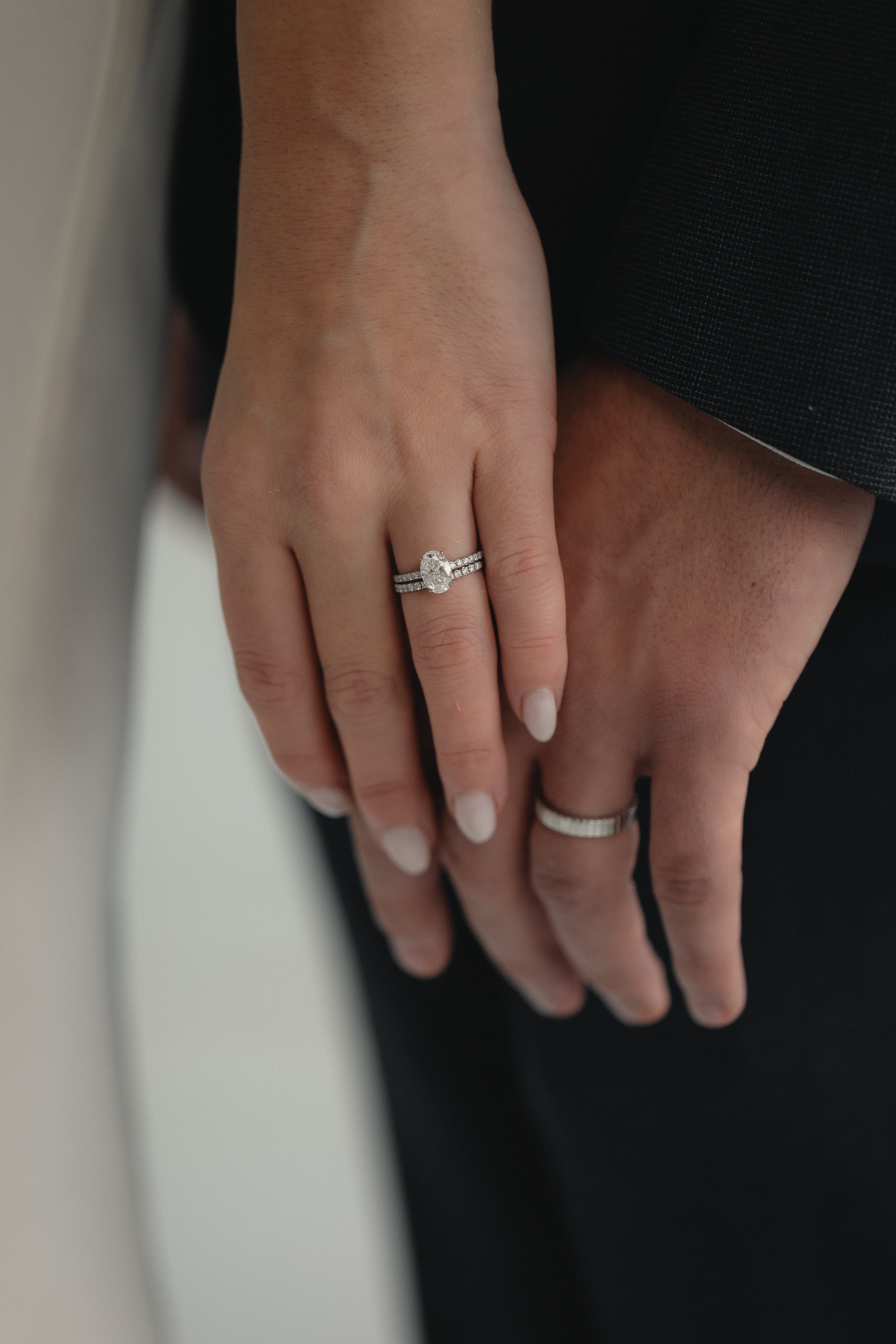 A close-up of a couple’s hands celebrating an engagement, featuring a KARAAT Oval Solitaire diamond ring with a pavé band in 18k yellow gold.