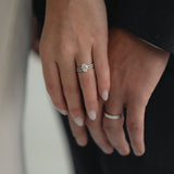 A close-up of a couple’s hands celebrating an engagement, featuring a KARAAT Oval Solitaire diamond ring with a pavé band in 18k white gold.