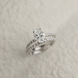 A professional still-life photograph of a KARAAT's oval-cut diamond solitaire engagement ring with a sparkling pavé band in 18k rose gold, displayed on a neutral background.