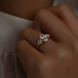Macro close-up of a model's hand with the KARAAT Oval Trilogy ring in 18k rose gold, highlighting the side-stone details.