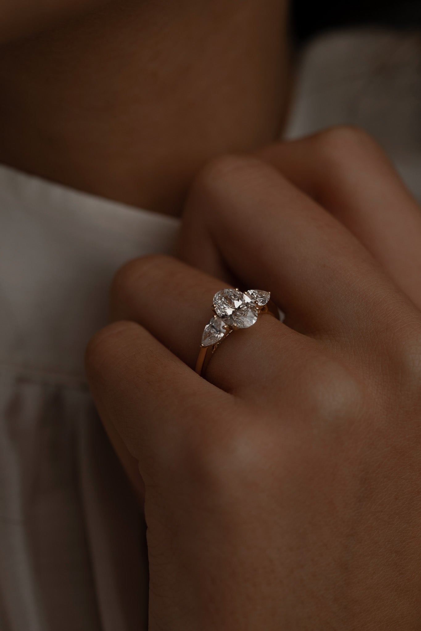 Macro close-up of a model's hand with the KARAAT Oval Trilogy ring in 18k rose gold, highlighting the side-stone details.