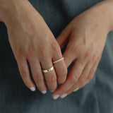 Detail shot of a model's hands gently clasped over a slate blue dress, showing a modern mixed stack featuring a wide solid gold band paired with the striking Pavé Diamond Ring III in white gold.