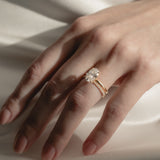 A soft-focus bridal image of a model's hand on shimmering white silk, showcasing a classic oval solitaire diamond engagement ring nested flush beside a delicate KARAAT pavé diamond wedding band.