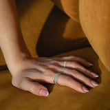 Sunlit detail shot of a model's hand resting on golden ochre fabric, showcasing a prominent ring stack featuring a thick diamond eternity band layered with a delicate classic gold pavé diamond ring.