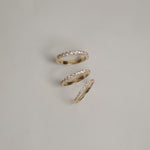 A clean flat-lay product shot displaying three KARAAT pavé diamond rings on a light grey background, showcasing different band widths and diamond carat sizes in polished yellow gold.