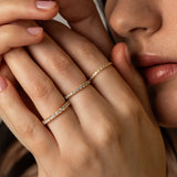 A close-up lifestyle shot of a model holding her hands up near her face, showcasing three delicate KARAAT pavé diamond rings stacked on different fingers in 18k yellow gold.
