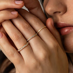 A close-up lifestyle shot of a model holding her hands up near her face, showcasing three delicate KARAAT pavé diamond rings stacked on different fingers in 18k white gold.