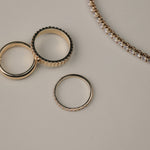 Rose gold diamonds rings on a light gray surface with a tennis bracelet next to them.