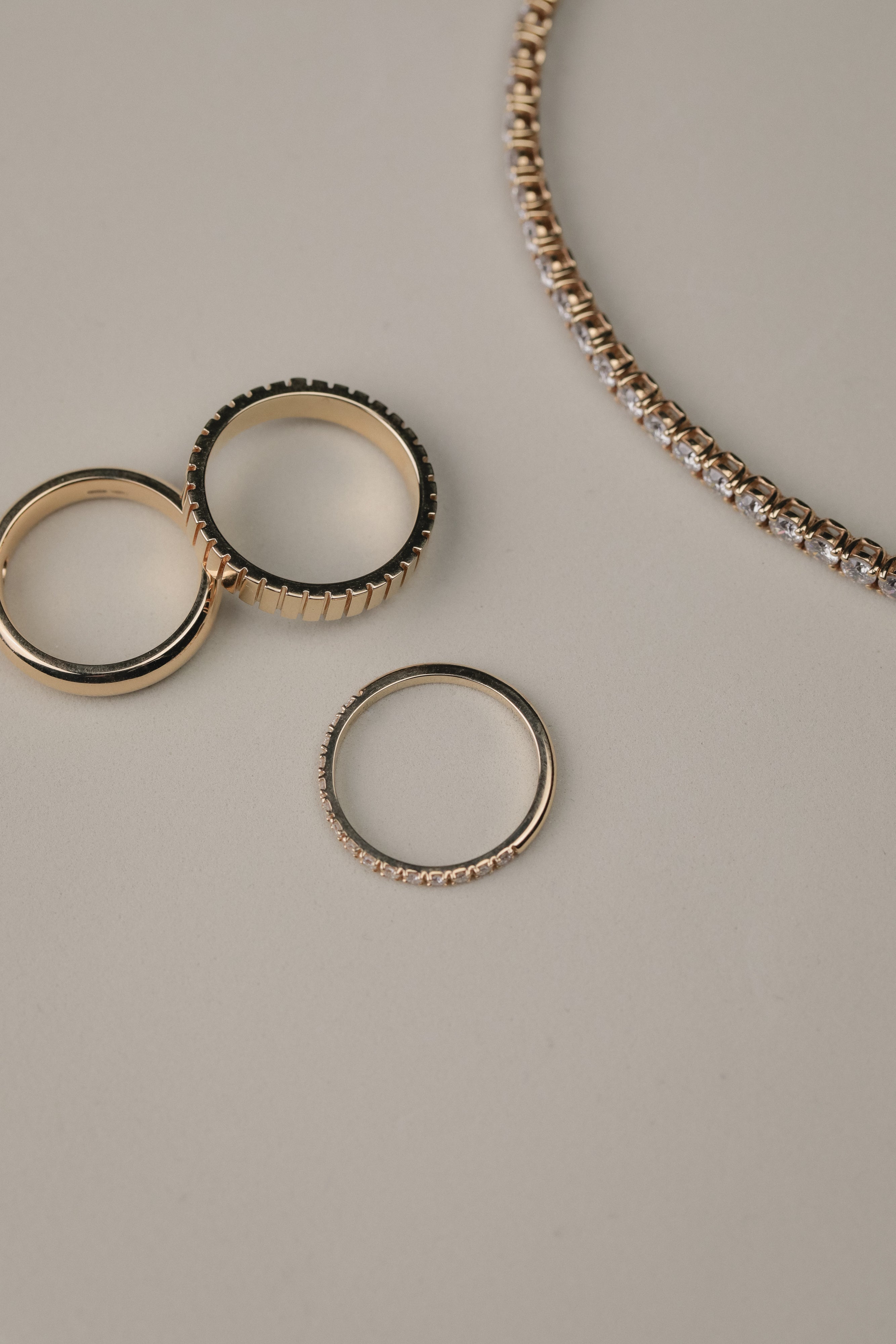 Rose gold diamonds rings on a light gray surface with a tennis bracelet next to them.