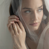 An editorial portrait of a bride looking through a sheer wedding veil, elegantly showcasing a KARAAT pear-shaped diamond solitaire engagement ring stacked with a matching white gold wedding band.