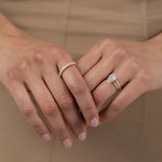 A close-up of a model's hands crossed against a beige dress, styled with a white gold KARAAT pear-shaped diamond solitaire ring stacked with a gold band on one hand, and a radiant-cut diamond half eternity band on the other.