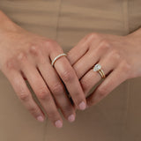 A close-up of a model's hands crossed against a beige dress, styled with a white gold KARAAT pear-shaped diamond solitaire ring stacked with a gold band on one hand, and a radiant-cut diamond half eternity band on the other.