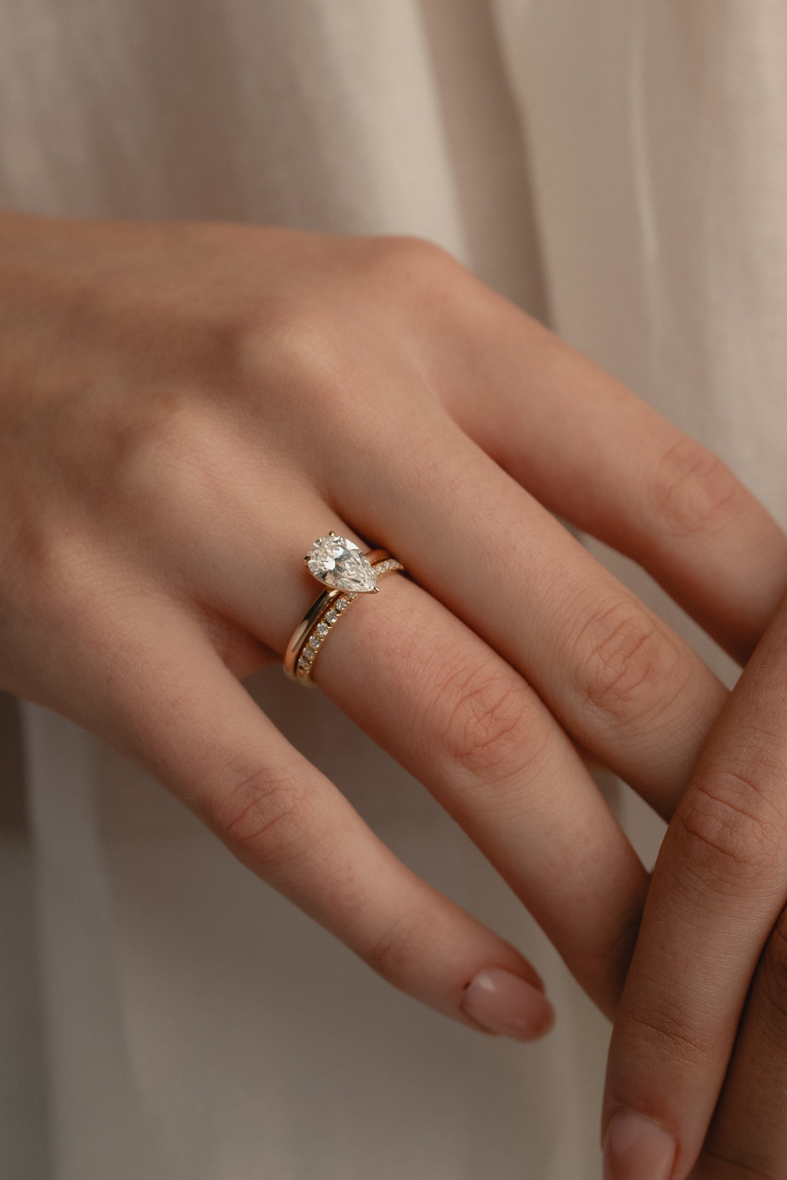 A detailed macro view of a yellow gold KARAAT pear-cut solitaire diamond engagement ring paired flawlessly with a sparkling pavé diamond wedding band on a model's hand.