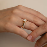 A soft-focus luxury bridal shot of a model's hand displaying a brilliant round solitaire diamond engagement ring nested flush beside the statement Pavé Diamond Ring III on a classic white gold band.