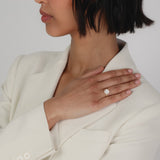 An elegant side profile of a bridal model wearing a tailored cream blazer, showcasing a rose gold KARAAT round solitaire diamond engagement ring with a brilliant halo setting on her finger.