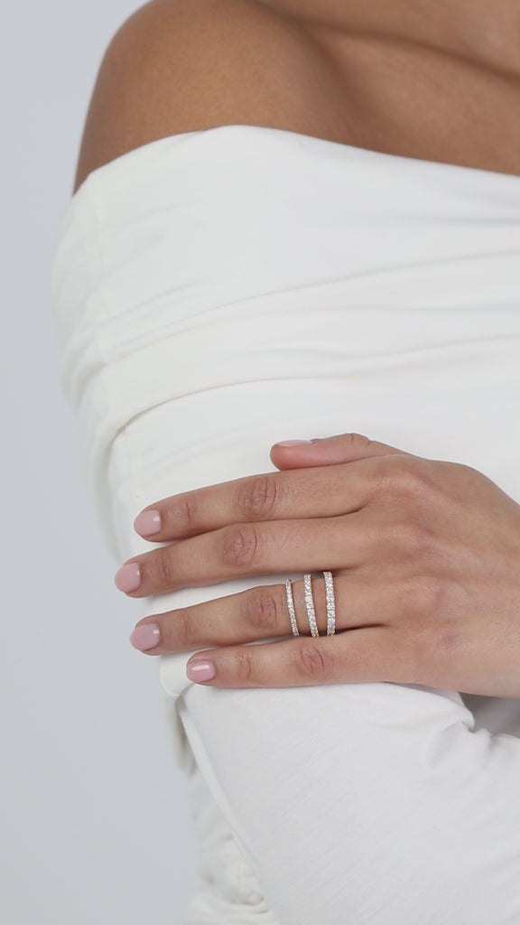 Close-up of a model wearing a crisp white top with her hands folded, elegantly displaying a modern three-layer ring stack composed of fine yellow gold KARAAT pavé diamond wedding bands.