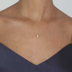 A lifestyle video displaying the delicate KARAAT diamond bezel solitaire necklace on a model's neckline, showcasing how the sparkling round-cut diamond catches the light against a fine gold chain.