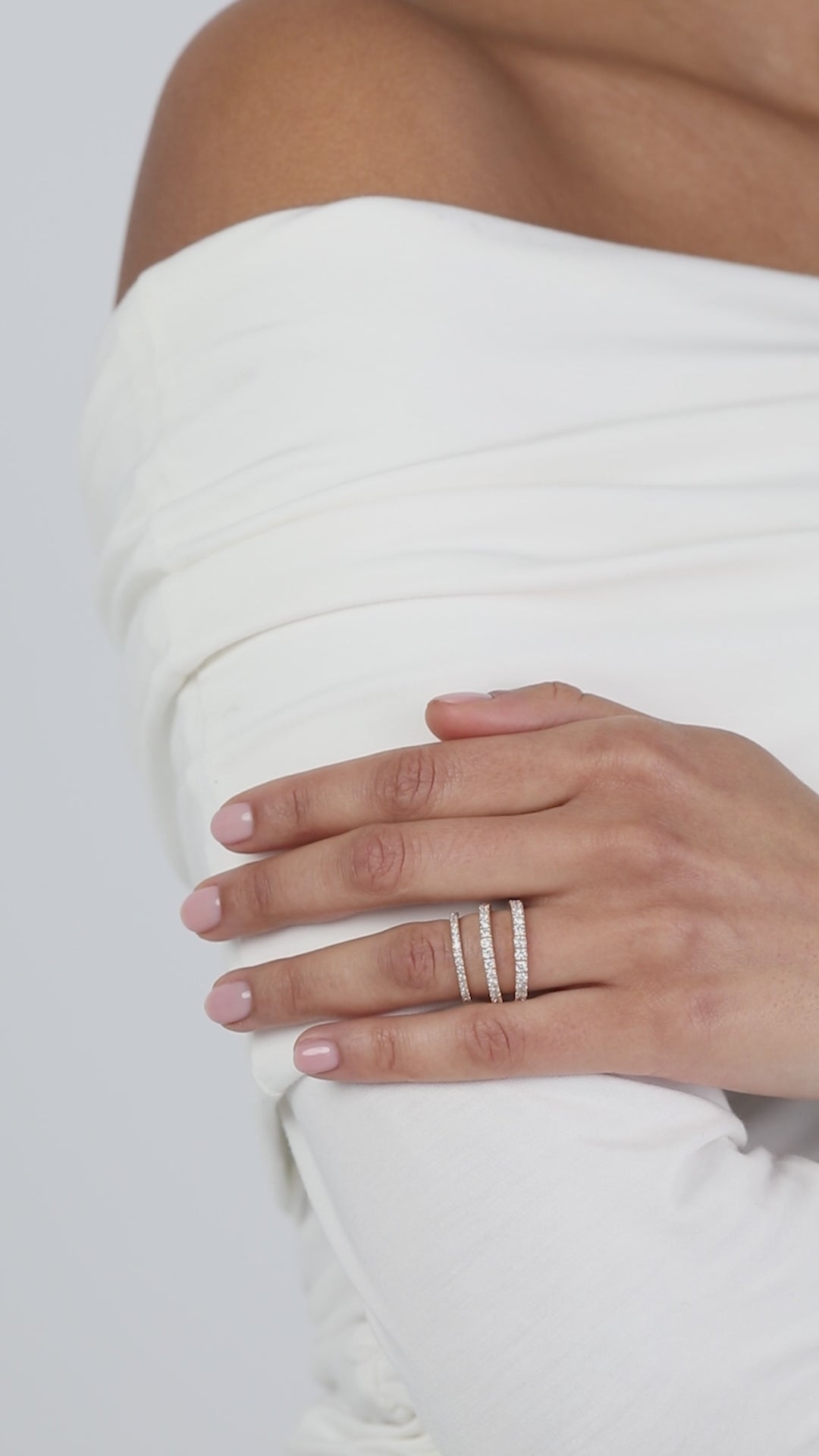 Close-up of a model wearing a crisp white top with her hands folded, elegantly displaying a modern three-layer ring stack composed of fine rose gold KARAAT pavé diamond wedding bands.