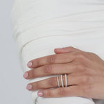 Close-up of a model wearing a crisp white top with her hands folded, elegantly displaying a modern three-layer ring stack composed of fine white gold KARAAT pavé diamond wedding bands.